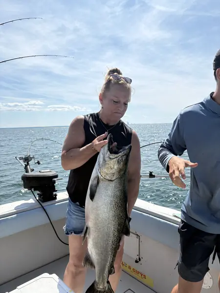 An angler holds up a large salmon on a charter boat on open water while a friend looks on