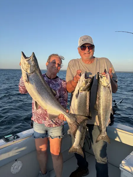 Two anglers on a charter boat holding three large salmon at sunset
