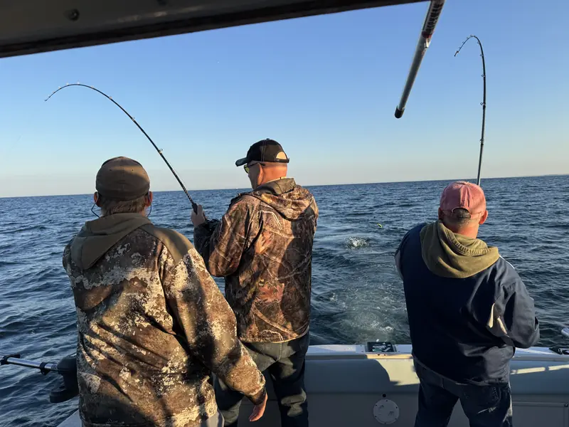 Three anglers fighting fish off the back of a charter boat on open water