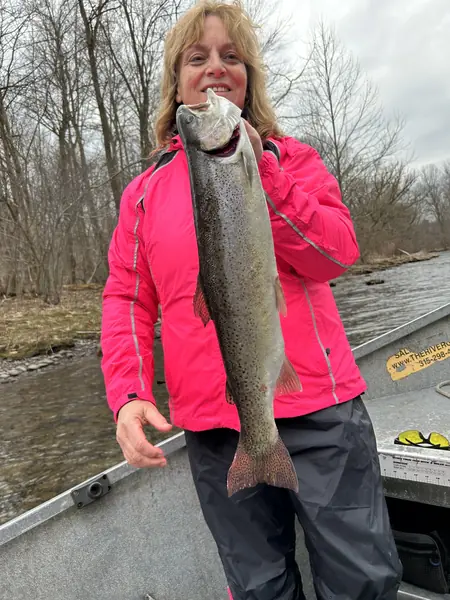Angler in a pink jacket holding a silver trout aboard a drift boat